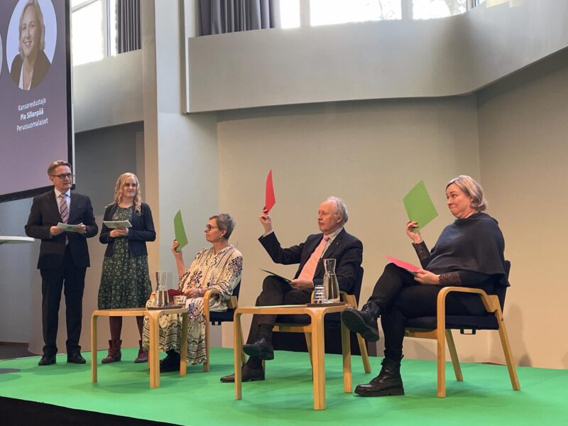 Panelistit äänestävät näyttämällä punaisia ja vihreitä lappuja.