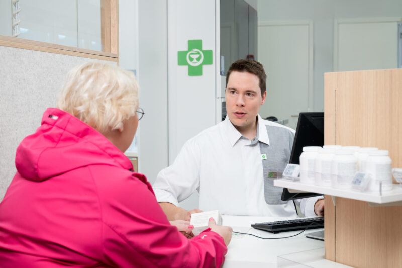 Iäkäs rouva ja apteekin farmaseutti apteekin palvelutiskin ääressä.